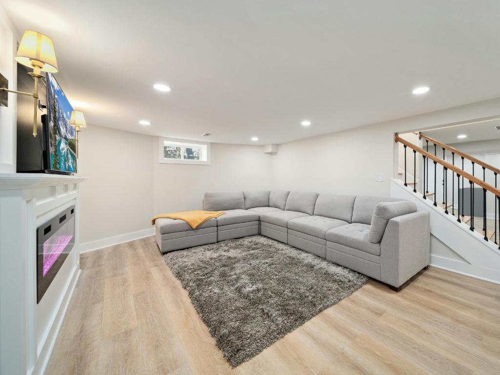 Basement entertainment space with large gray couch and electric fireplace in a Perkasie home by Metzler Construction - Stock Image